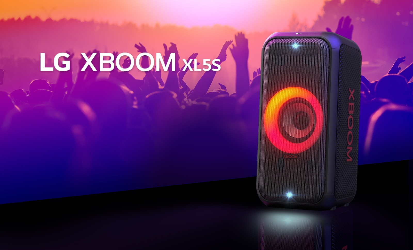 LG XBOOM XL5S padėtas ant scenos ir jame įjungtas raudonos bei oranžinės spalvų pereinantis apšvietimas. Už scenos žmonės mėgaujasi muzika.