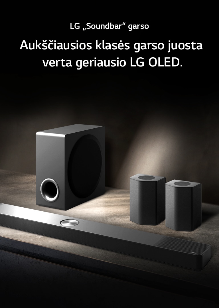 LG „Soundbar“ ir galiniai bei žemųjų dažnių garsiakalbiai išdėstyti kampu ant rudos medinės lentynos, juodoje tamsos apgaubtoje patalpoje, su vienintele šviesa, sklindančia virš garso sistemos.