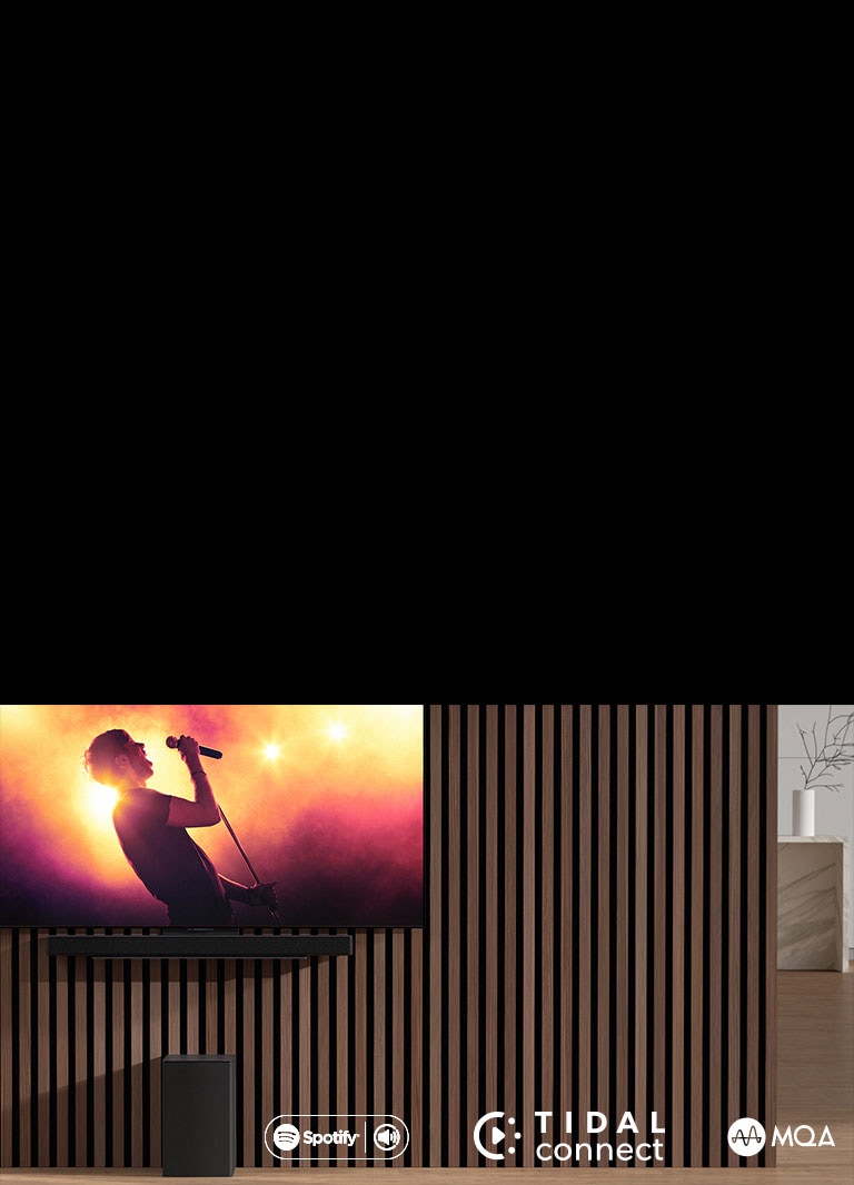 Ant sienos LG OLED C, o žemiau – „LG Sound Bar SC9S“, įrengtas ant išskirtinio laikiklio. Po juo – žemųjų dažnių garsiakalbis. Televizoriuje rodoma koncerto scena.