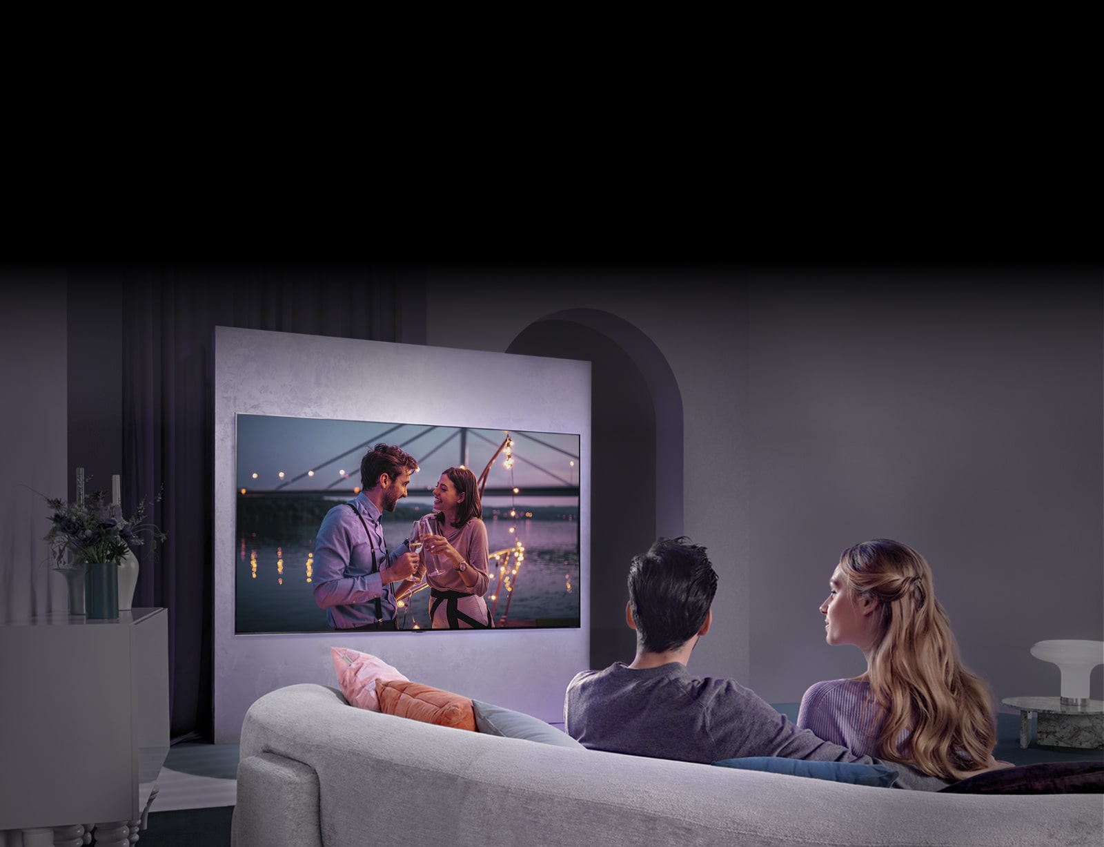 Cilvēks, kurš sēž uz dīvāna un bauda filmu uz liela televizora, kas piestiprināts pie sienas.