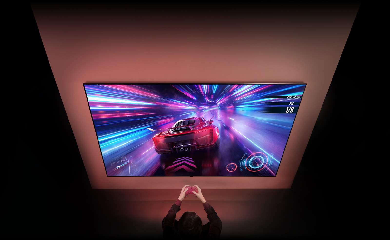 Redzams liels televizors pie sienas un sacīkšu spēles ekrāns. Televizora priekšā var redzēt rokas un kontrolierus, personai koncentrējoties uz spēli.