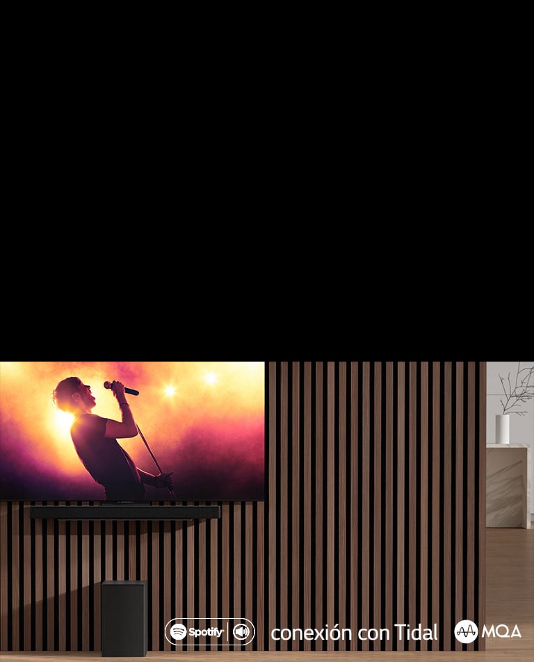 LG OLED C ir piestiprināts pie sienas, zem tā uz ekskluzīvā kronšteina ir piestiprināts LG Sound Bar SC9S. Zemo frekvenču pastiprinātājs ir novietots zem tā. TV ekrānā redzama koncerta aina.