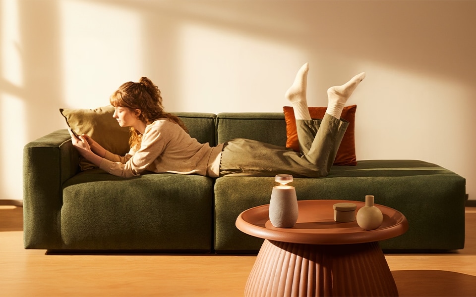 woman enjoying on the sofa the sound of LG XBOOM 360 portable, bluetooth, wireless speakers with 3-way surround sound system