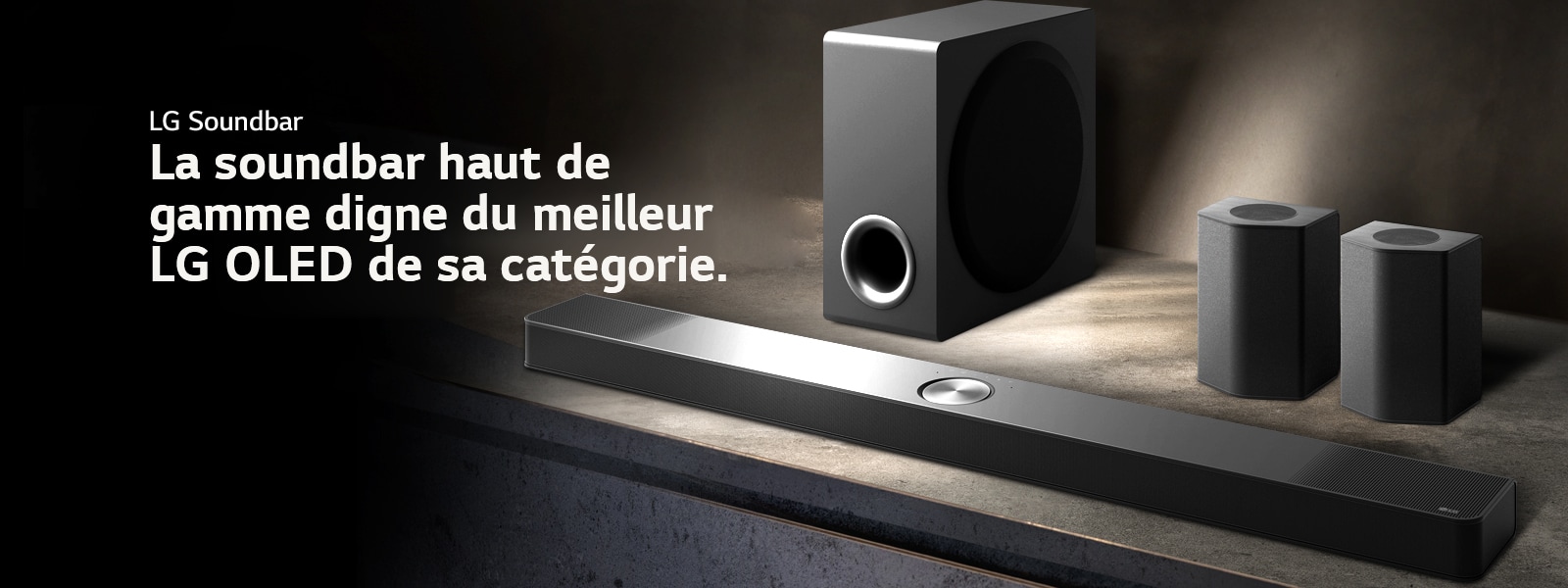 LG Soundbar, enceintes arrière et caisson de basse installés en biais sur une étagère en bois marron dans une pièce obscure, avec une lumière qui n’éclaire que le système audio