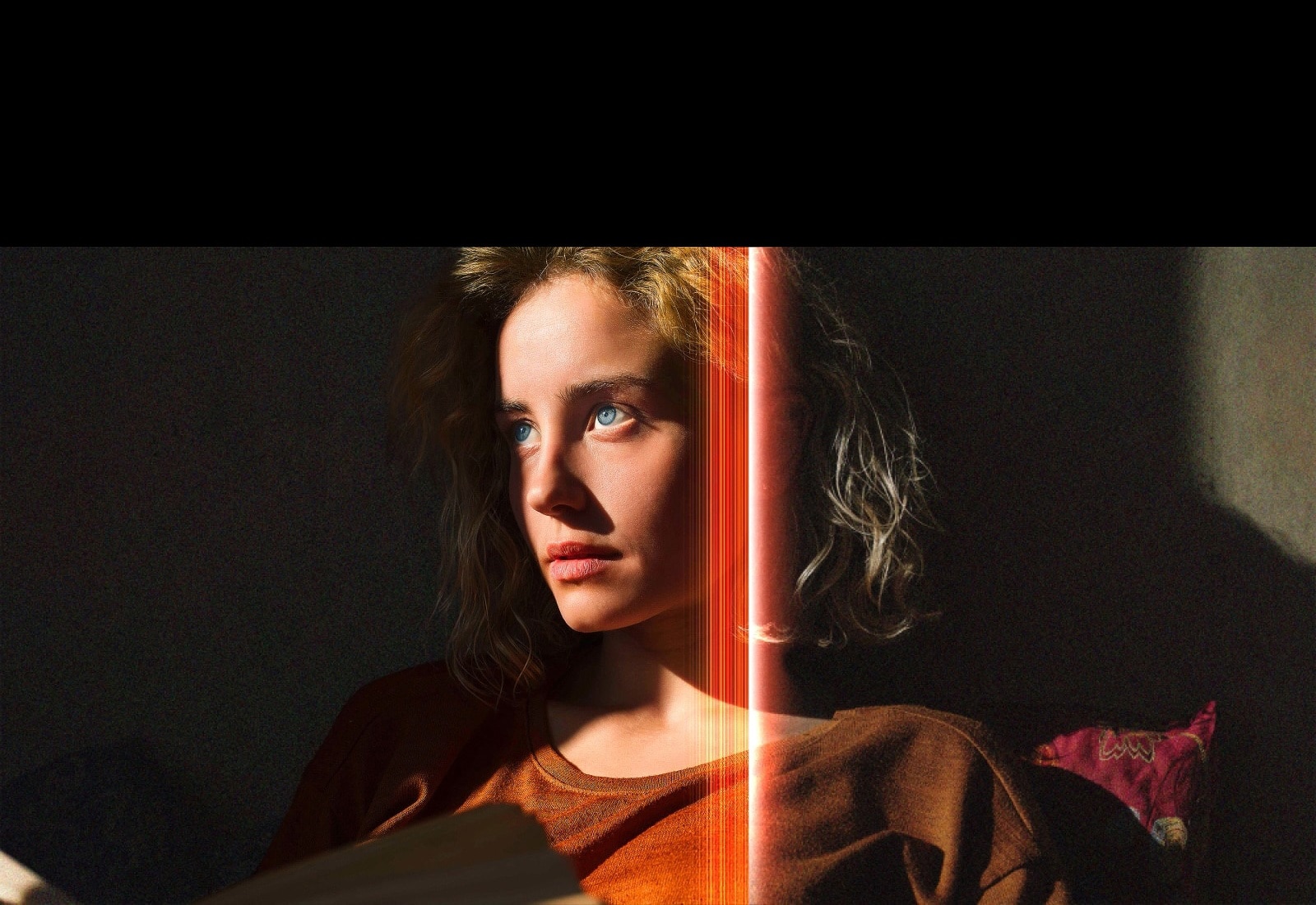 An video of a woman with piercing blue eyes and a burnt orange top in a dark space. Red lines depicting AI refinements cover part of her face, which is bright and detailed, while the rest of the image looks dull.	