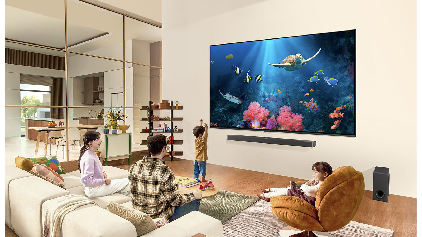 An image of a family in a living room with an ultra big LG TV mounted on the wall, with an ocean scene including coral and a turtle on the screen.