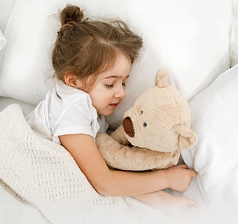 A little girl is lying in bed with a doll in her arms