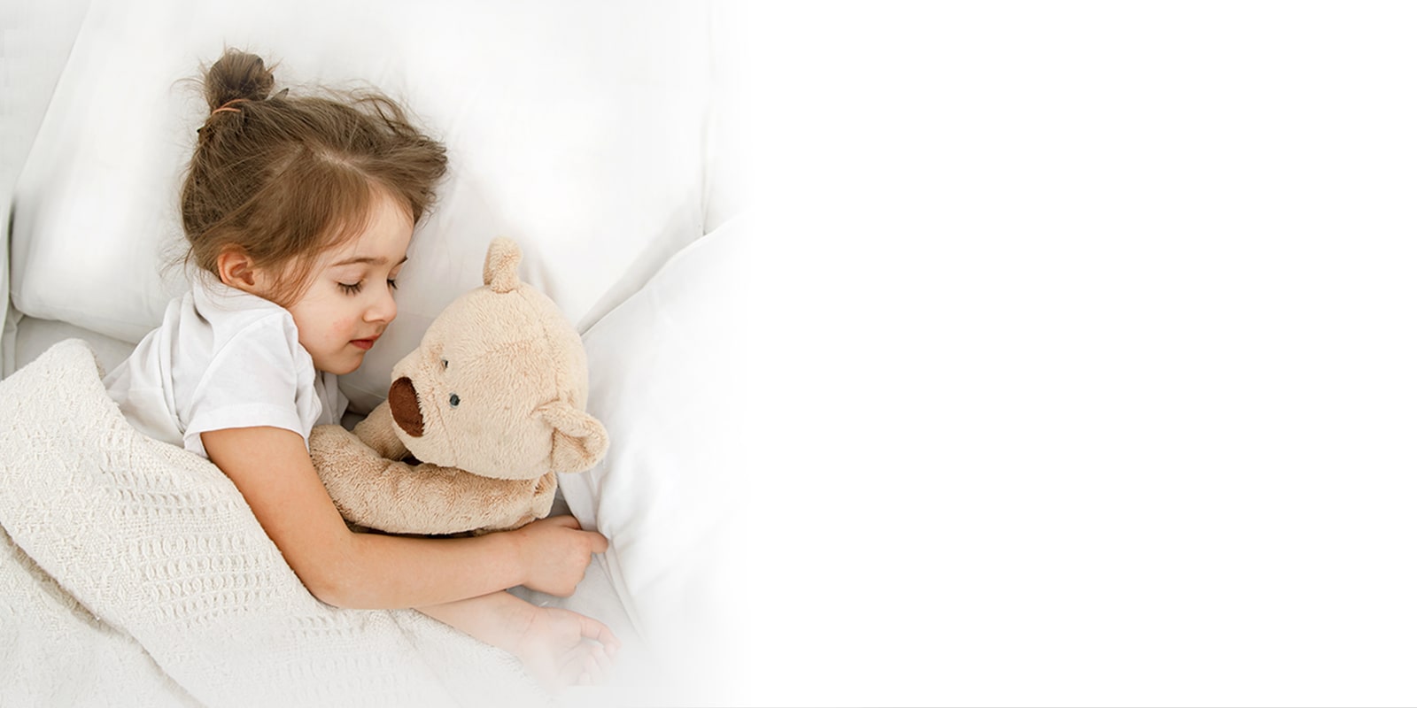 A little girl is lying in bed with a doll in her arms