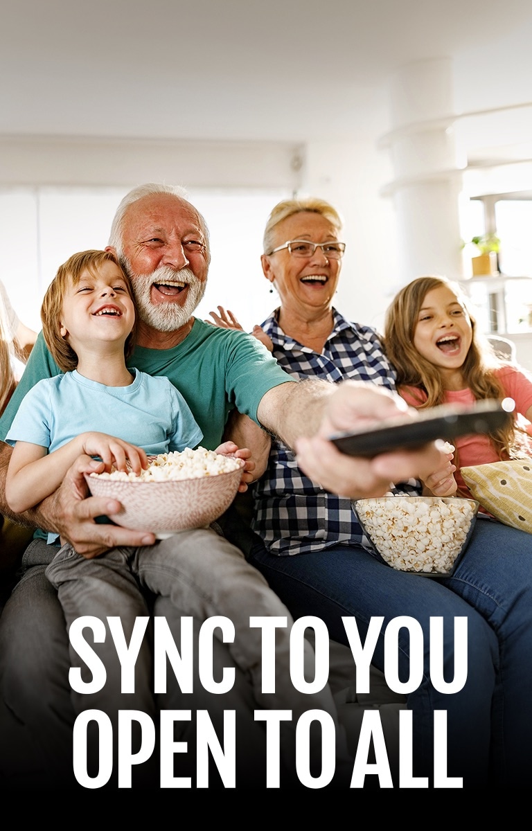 A family sits laughing while the grandfather points the remote outward. 