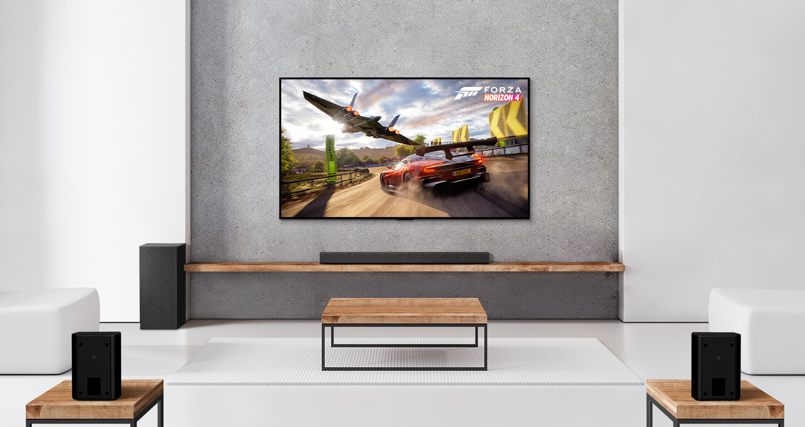 A set of 2 rear speakers, subwoofer, a soundbar, and TV are in a white living room. A driving car and a spaceship are on TV screen. 