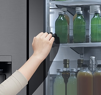 The front view of a black glass InstaView refrigerator with the light on inside. Hands tapping on InstaView screen.