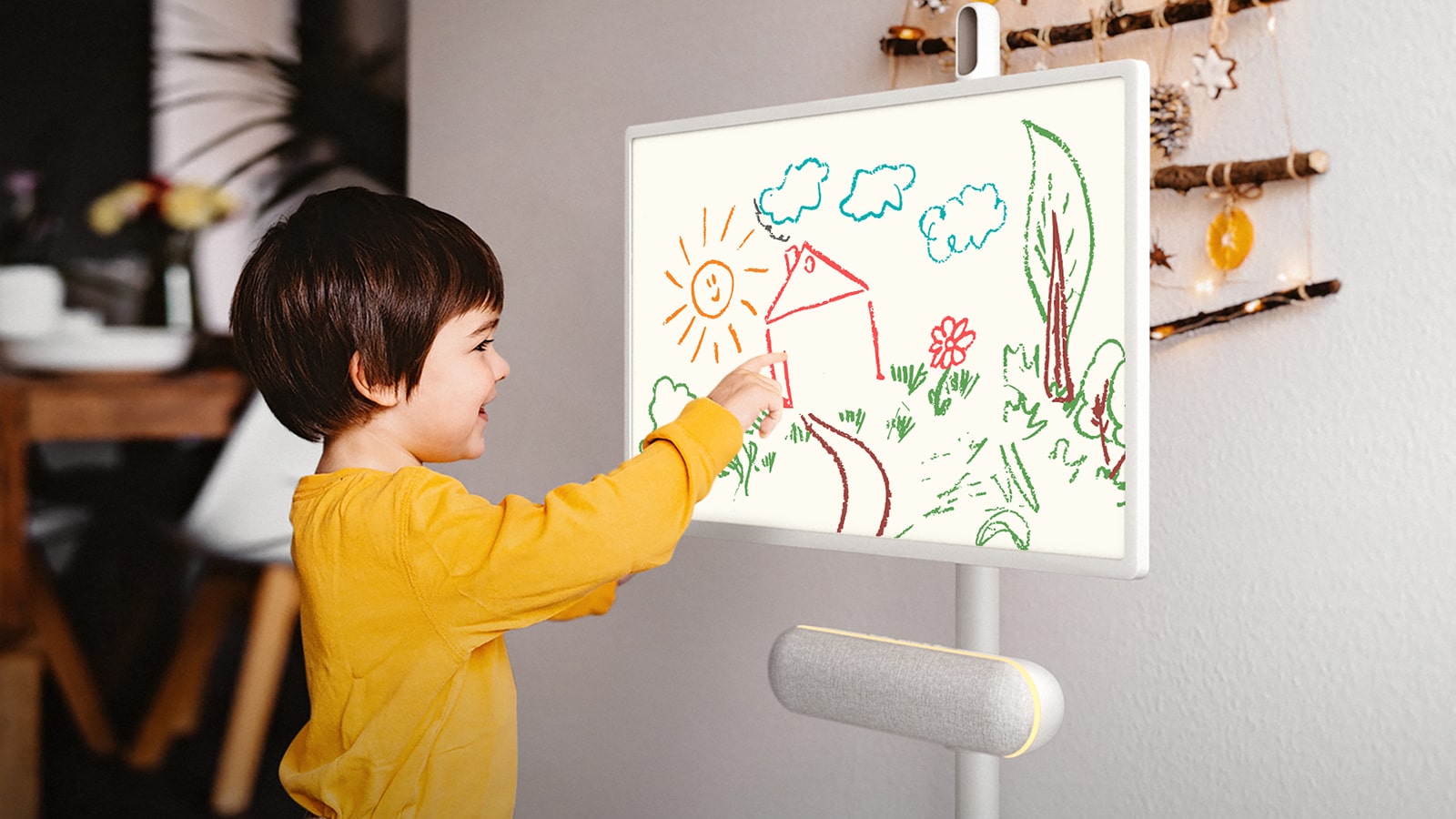 The LG StanbyME is placed in the kitchen with the XT7S speaker attached. A child draws on the screen, and the speaker's yellow mood lighting is on.