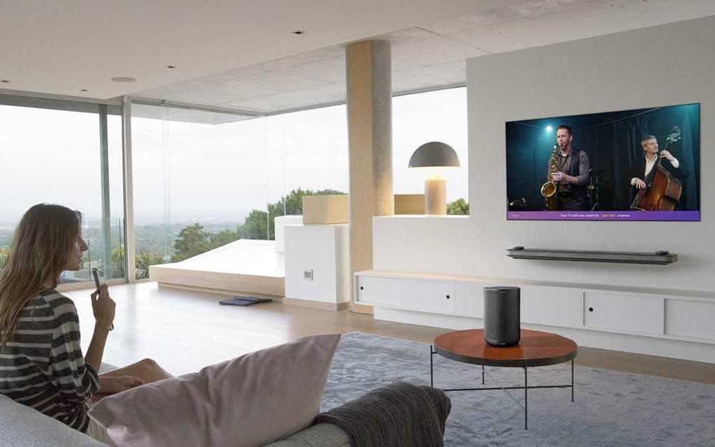 Uma mulher sentada na sua sala de estar, a falar com a sua LG OLED TV Wallpaper através do LG magic remote.