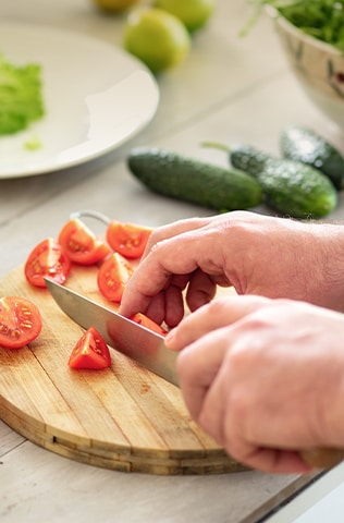 'Image of cutting tomatoes on a cutting board with a knife.