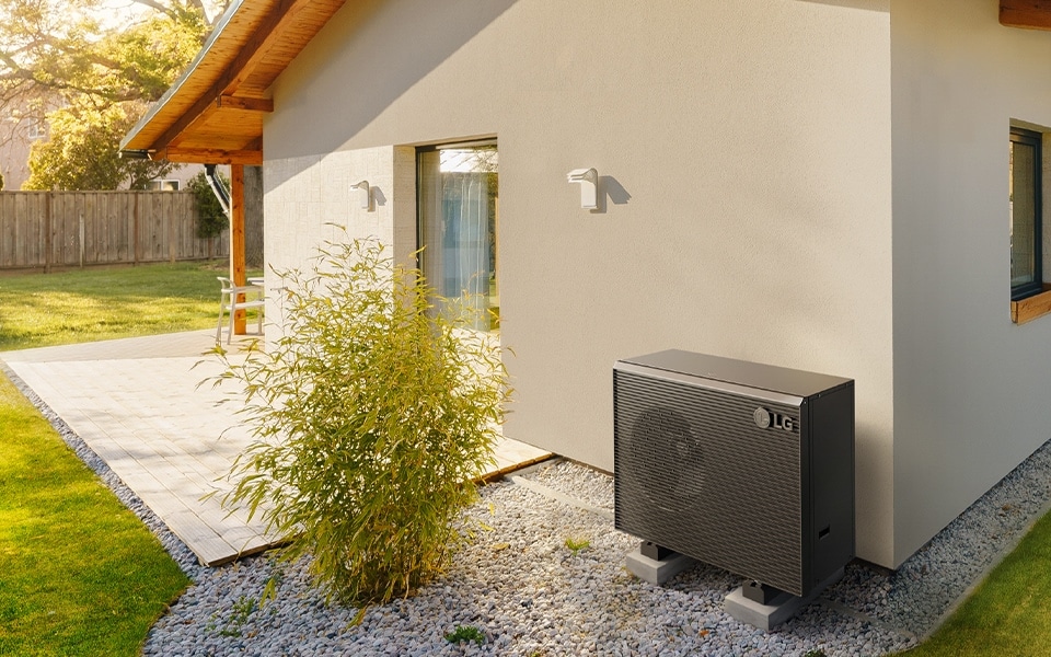 Therma V R290 Monobloc Heat Pump installed in a garden beside a house wall, showcasing its sleek design and functionality.