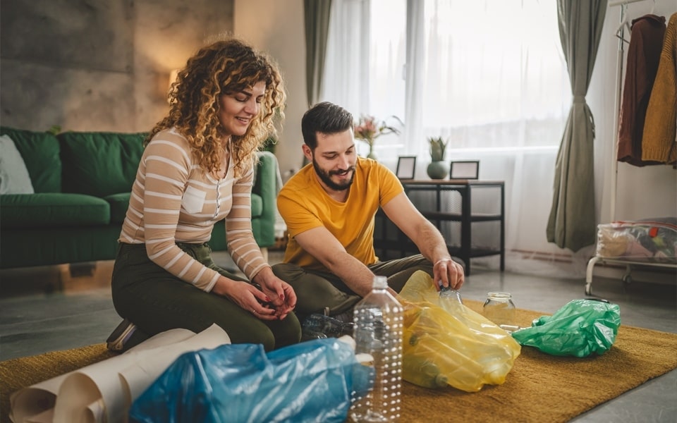 Cuplu care separă materialele reciclabile (pungă de plastic, sticlă de plastic și hârtie)