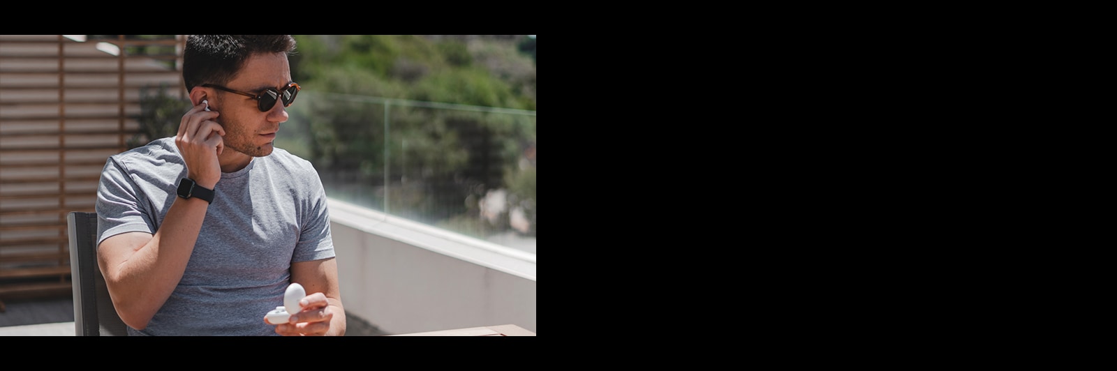 Изображение человека в темных очках, вынимающего вкладыш из уха на балконе при дневном свете