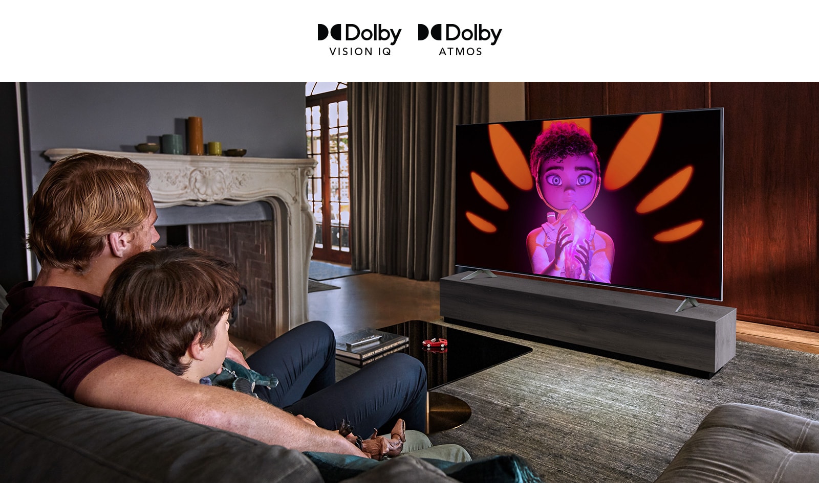 Расположенные по горизонтали логотипы Dolby Vision IQ и Atmos. Под логотипами показаны отец и сын, сидящие на диване и смотрящие телевизор, на котором показана девочка, держащая минерал по центру черно-оранжевого фона.