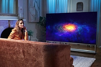 Оливия Палермо отдыхает на диване и смотрит OLED-телевизор LG SIGNATURE 8K.