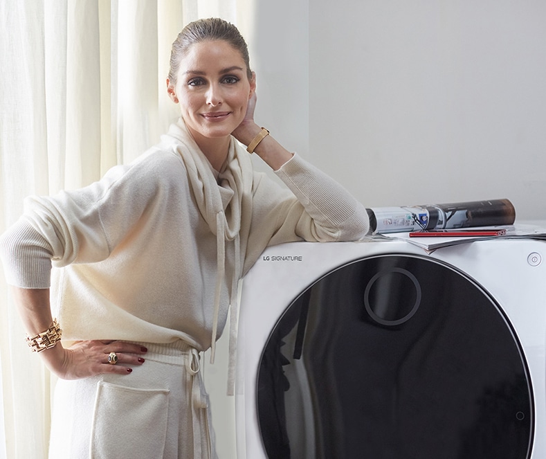 Оливия Палермо стоит, облокотившись на стиральную машину LG SIGNATURE.