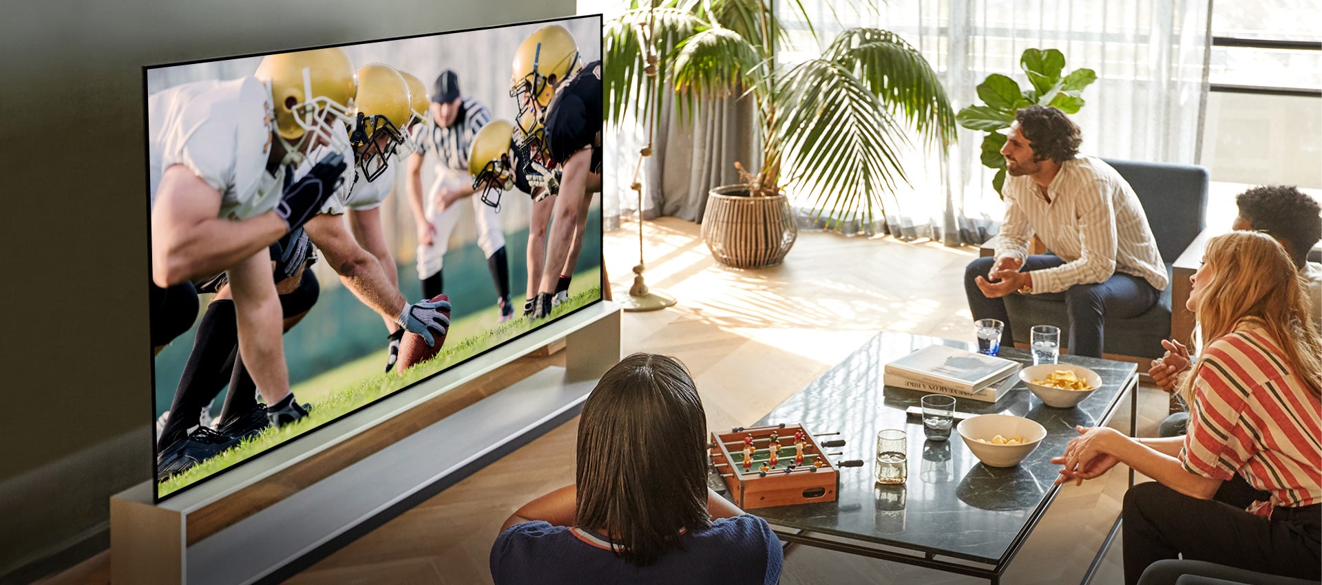 In the living room, a group of friends sitting with a wide viewing angle and watching a football game on TV