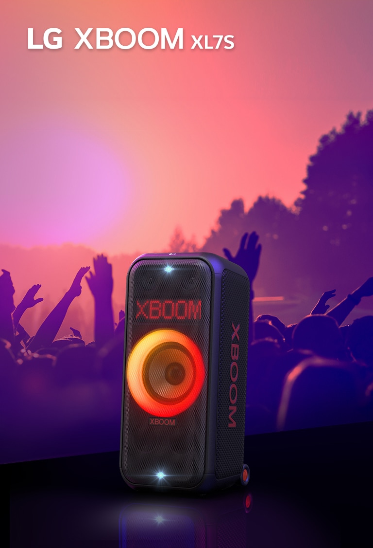LG XBOOM XL7S umiestnený na pódiu so zapnutým červeno-oranžovým osvetlením. Za pódiom si ľudia užívajú hudbu.
