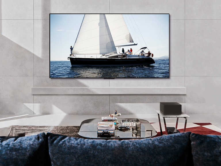白天時間位於現代客廳空間的 LG OLED evo M4 和 LG Soundbar。以理想亮度顯示帆船航行於海洋中的螢幕影像。
