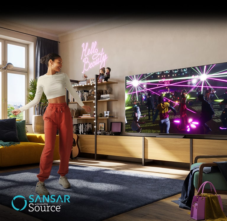 Жінка танцює у своїй кімнаті й дивиться концерт у метавсесвіті Sansar на екрані телевізора.