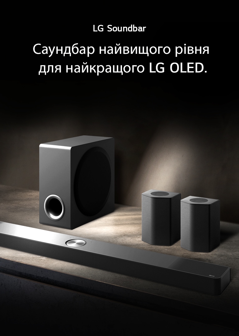 LG Soundbar, задні динаміки та сабвуфер (вигляд під кутом) на коричневій дерев’яній полиці в чорній кімнаті, огорнутій темрявою, де світло падає лише на звукову систему.
