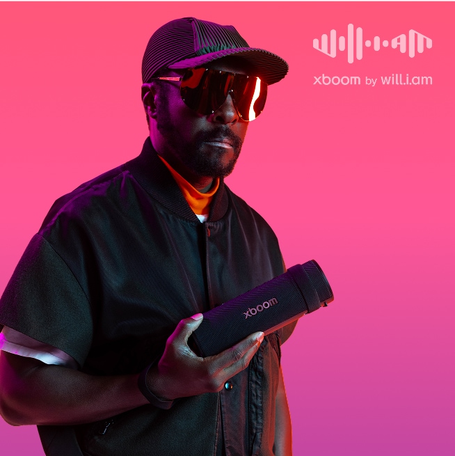 will.i.am dressed in black and wearing sunglasses holds an LG xboom speaker against a pink gradient background. will.i.am logo with the label 'xboom by will.i.am.'