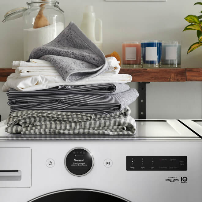 A pile of towels sits on top of a front-load washer in a laundry room.