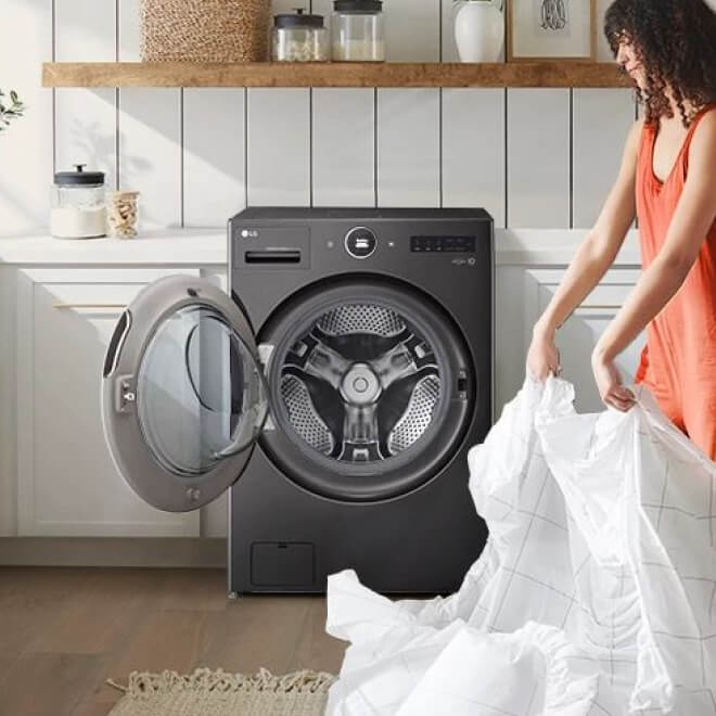 A woman is standing to the right of an all-in-one washer/dryer with a fitted sheet in her hands.