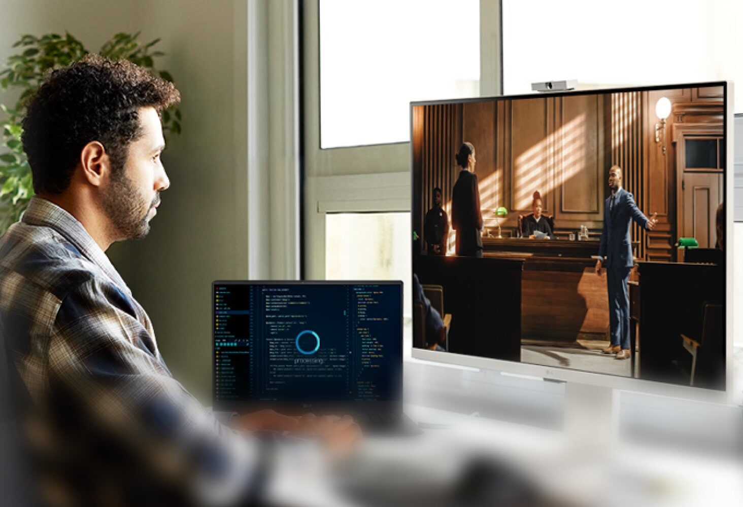 Man multi-tasking with two screens. One displays a TV show, the other a workspace.