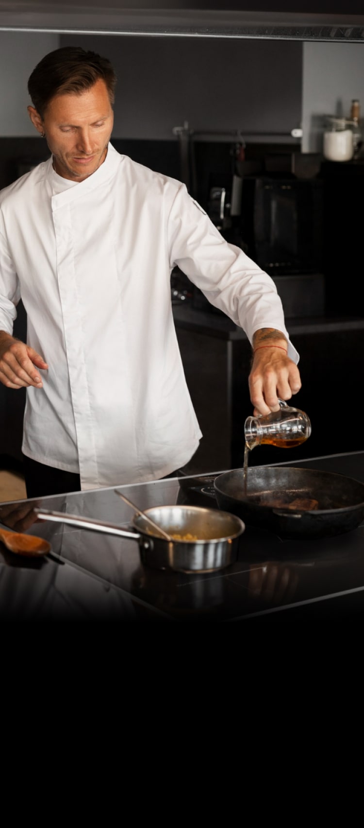 A professional chef is cooking with an induction range in a restaurant kitchen with a sous chef preparing food behind him.