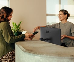 Friendly receptionist showing a woman where to sign on a digital tablet.