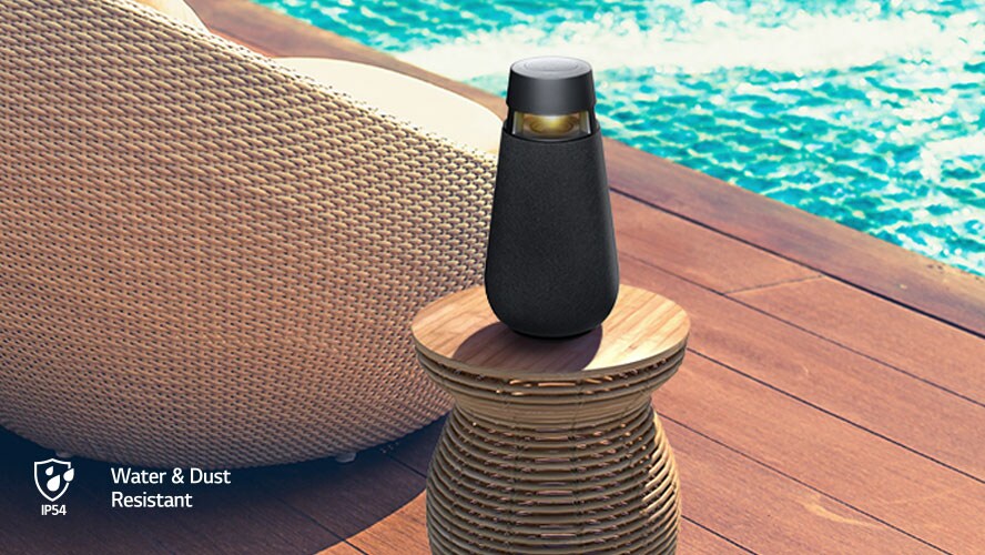 The LG XBOOM 360 Speaker on a table next to a pool on a sunny day.