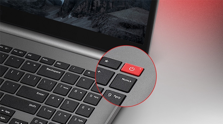 This image shows a close-up of a laptop keyboard. The focus is on a distinctive red power button located in the upper-right corner, highlighted with a circular zoom effect. 