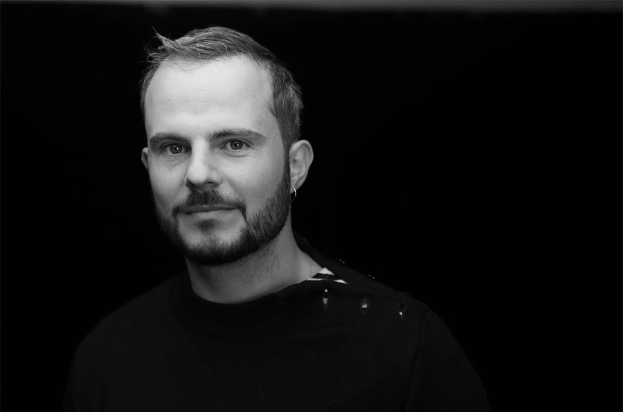 An upper-body portrait of Yoann Bourgeois as he smiles against a black background.