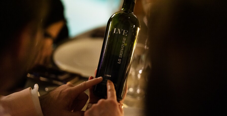 A bottle of LG SIGNATURE X LVE wine is held in people's hands.