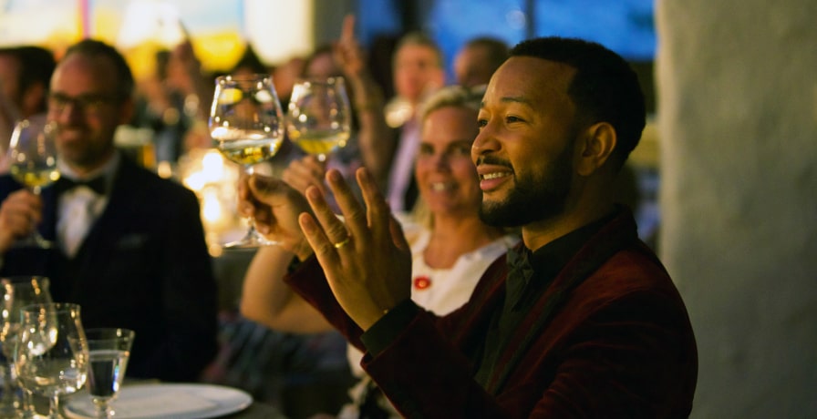 John Legend sits in the audience and makes a gesture in 