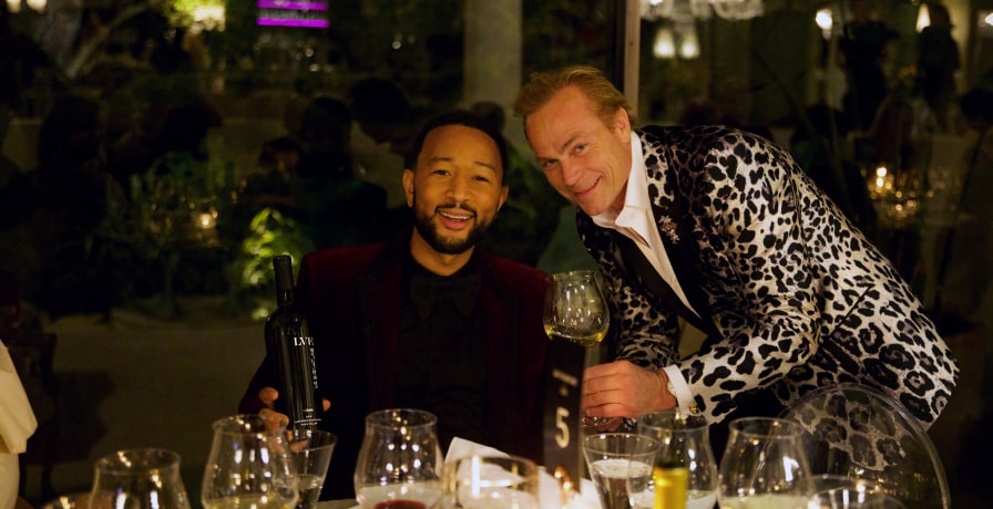 John Legend and Jean-Charles Boisset looks into the camera at the dinner table.