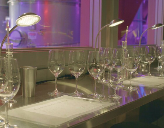A bar table stacked with empty wine glasses, lamps, and a huge screen on the back wall.