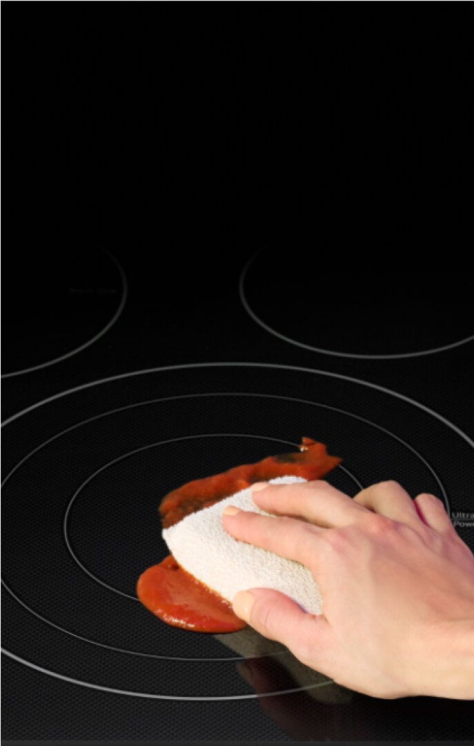 A hand wiping up a red sauce spill on an LG EasyClean® cooktop, demonstrating how easily the cooktop can be cleaned.