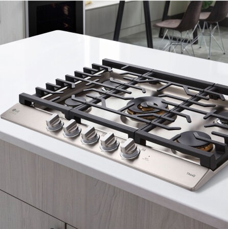 A gas cooktop with five burners and stainless steel knobs, showcasing a sleek design with detailed precision controls.