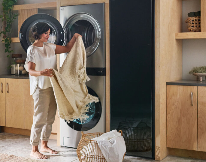 Woman loading a blanket into an LG Studio WashTower laundry unit in a bright, modern laundry room.