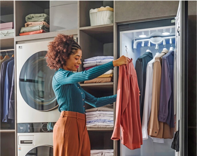 Woman hanging clothes inside the LG Styler wardrobe, showcasing its large capacity.