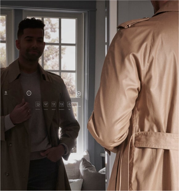 Man looking into a full-length LG Studio Styler mirror while dressed in a beige trench coat.