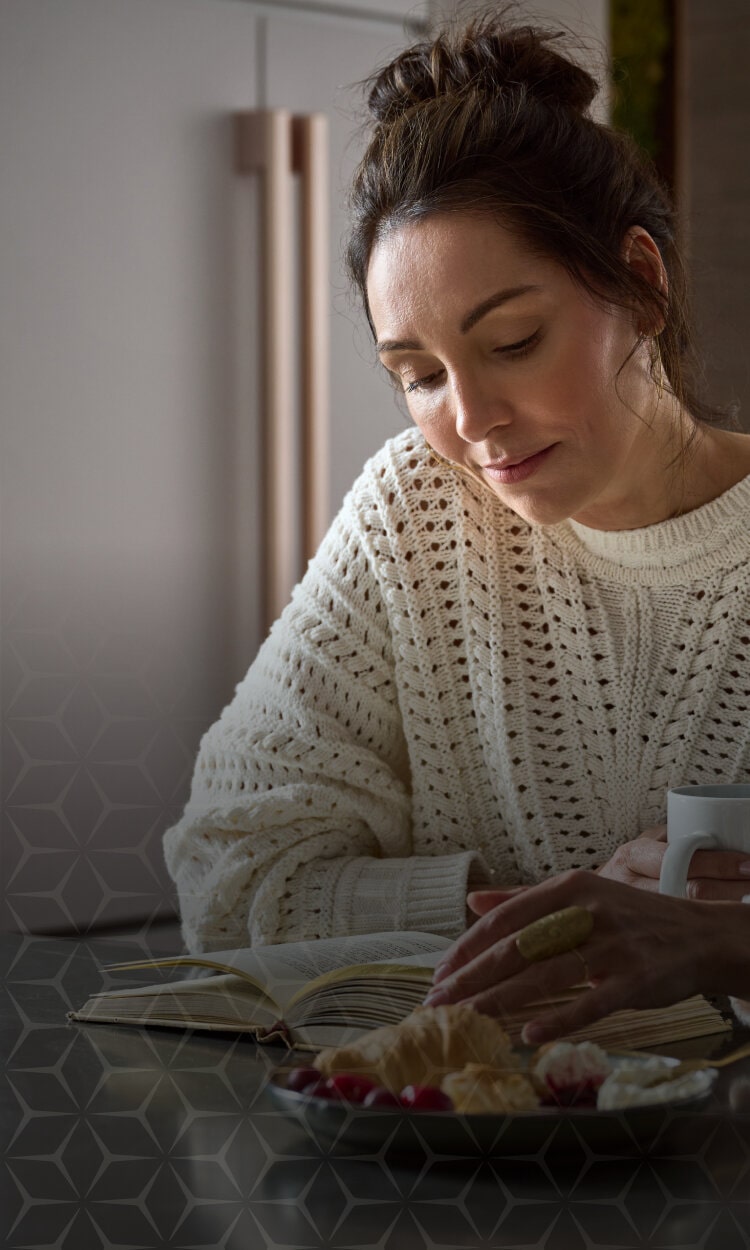 Woman reading a book with a mug, promoting LG Studio design-inspired refrigerators.