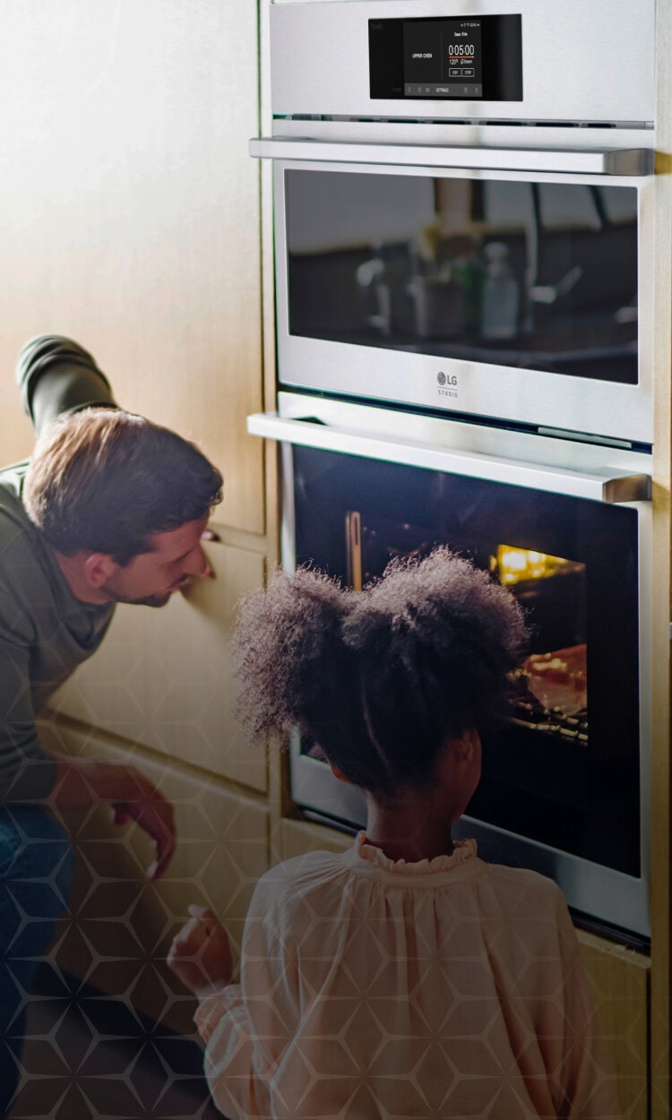 A man and a young girl watching food cook in an LG Studio wall oven. The oven's sleek, stainless-steel finish blends seamlessly into the kitchen cabinetry. The scene emphasizes the oven’s built-in beauty and family-friendly design.