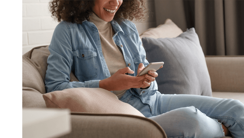 Woman Sitting on Couch Smiling While Registering for an LG Premium Care Plan From Her Phone.